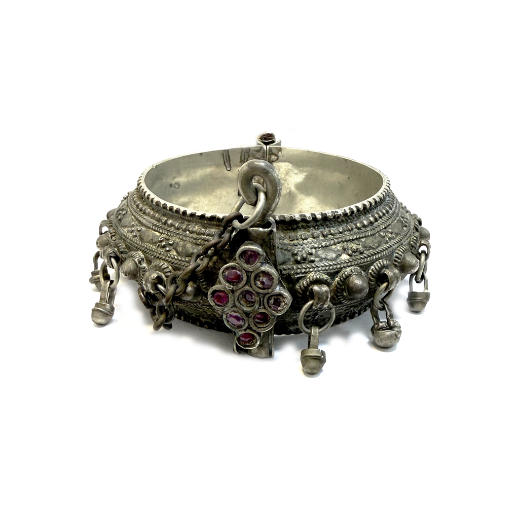 Antique Arabian silver hinged bangle with bell drops and garnet clasp, angled view